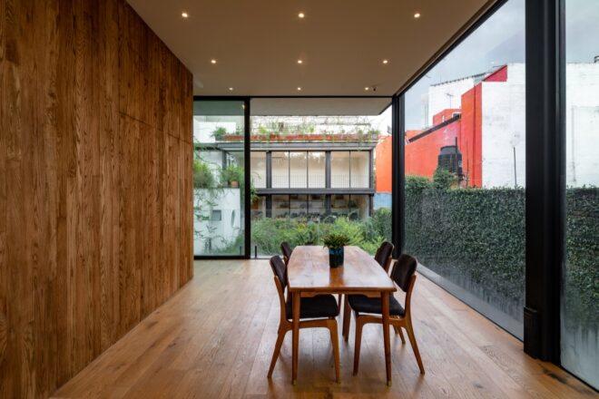 A meeting room with a table and chairs. To the left is a wooden wall, while all other walls in the room are glass, looking out onto greenery outside.