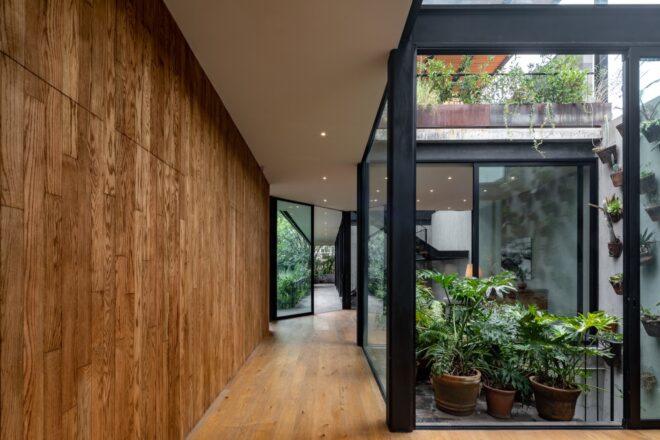A wood hallway flanked by glass walls on one side, with potted plants outside.