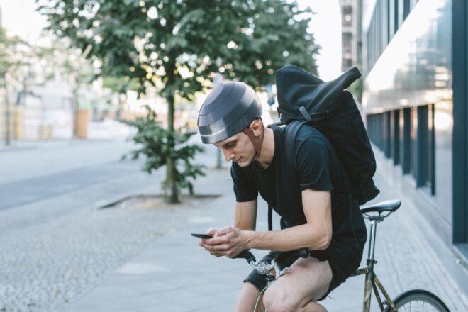 A person sitting on a bicycle, wearing a helmet and checking their phone.