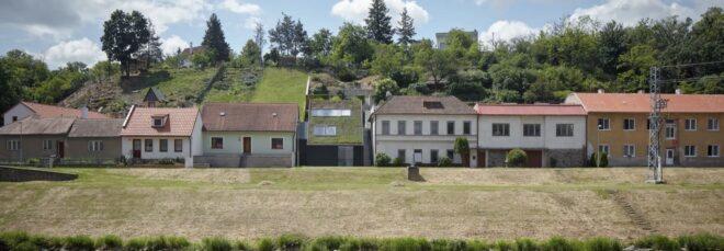 black home with green roof surrounded by beige homes