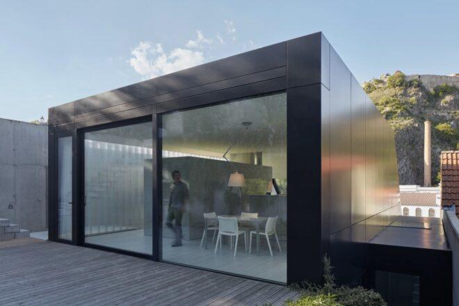 black metal home with sliding glass door leading to wood patio