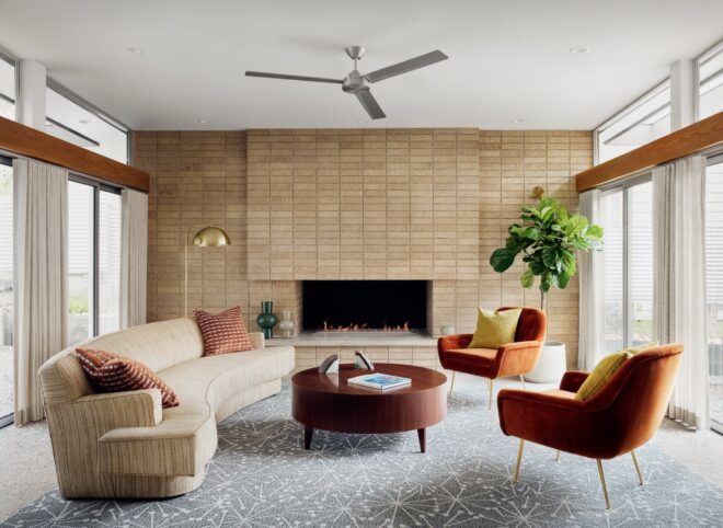 living room with brick wall and curved, beige sofa facing orange chairs