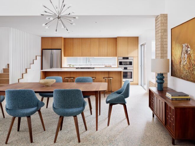 wood dining table with blue chairs near a kitchen with wood cabinets
