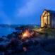A night view of a gabled home on a rocky cliff.
