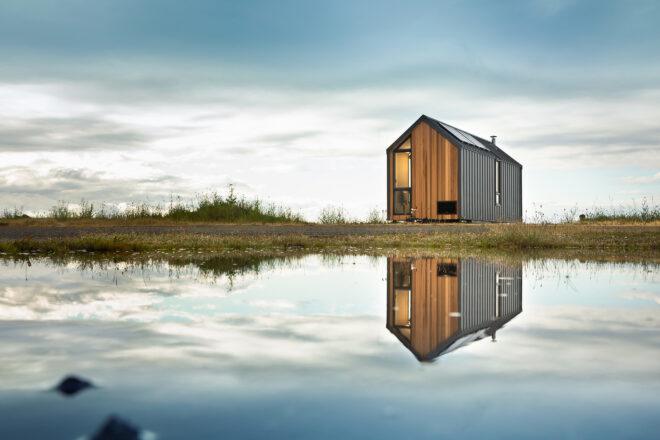 A traditional gable-roofed house reflected in the water of a lake.