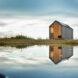 A traditional gable-roofed house reflected in the water of a lake.