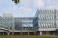 A streetview of a glass facade building with an elevated bridge connecting to it.