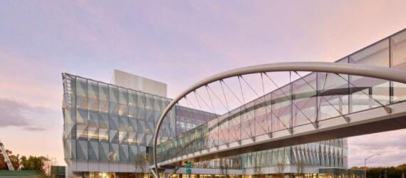 A streetview of a glass facade building with an elevated bridge connecting to it.
