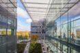 An L-shaped glass facade building with greenery and trees below in a courtyard area.