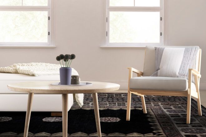 A wood frame chair with off-white cushions in a living room next to a round coffee table.