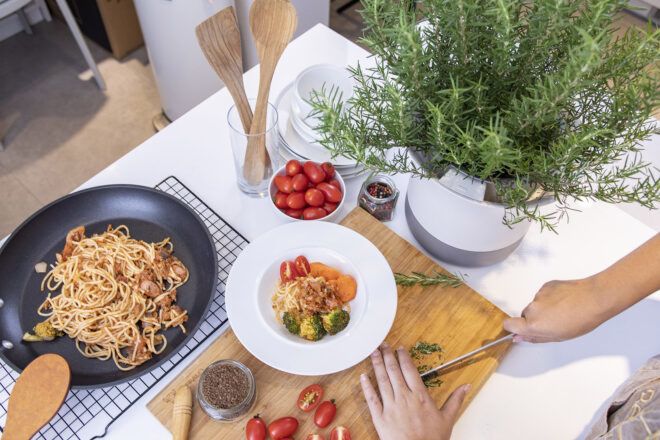 A person cooking in the kitchen next to a potted herb.