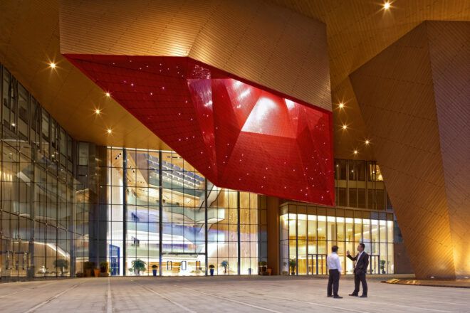 people standing underneath a red-framed, geometric skylight