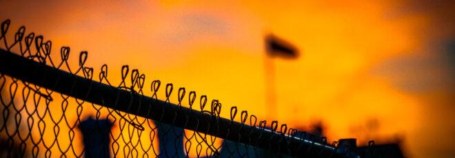 A close-up of a border fence with a flag in the background.