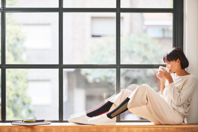 person sipping coffee and wearing compression socks while sitting near large window