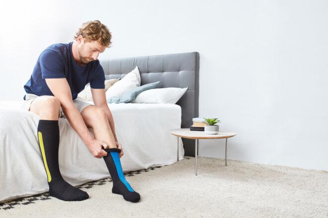 person sitting in bed pulling up compression socks