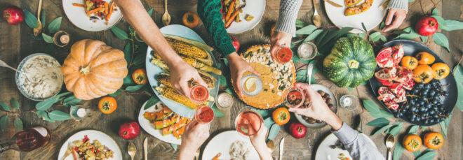 people toasting with drinks over a table of plant-based dishes