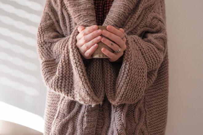 person in brown sweater holding a cup of coffee