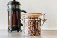 glass jar of coffee beans next to French press