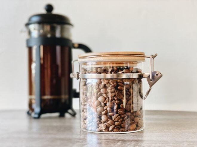 glass jar of coffee beans next to French press