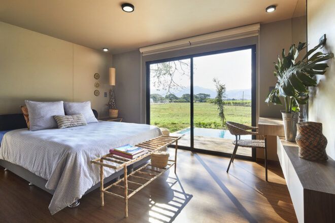 A bedroom with a large sliding glass door, wood floors and a bed covered in white sheets.