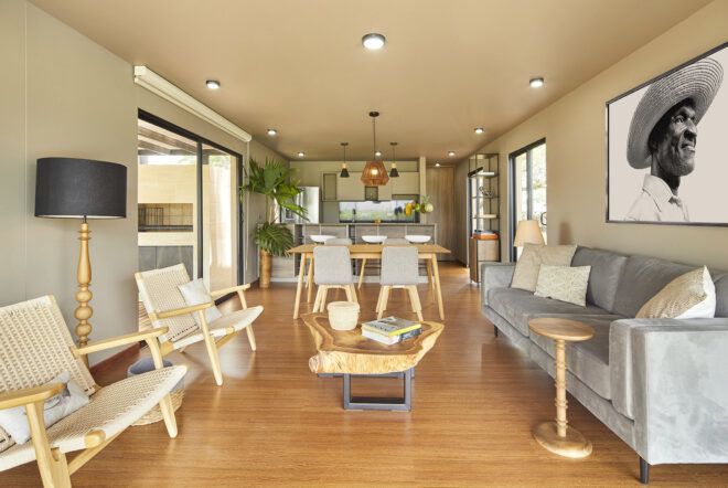 A living room with wood chairs and coffee table. A light blue/gray sofa sits on the right side of the room.