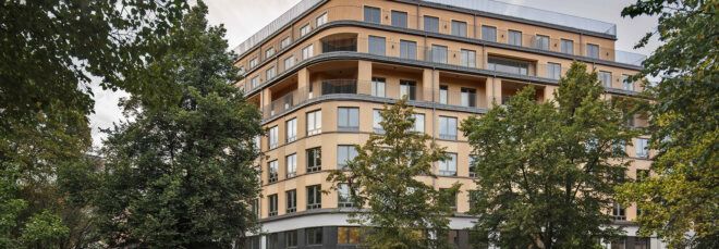A streetview of an apartment complex with a light brown colored facade and windows.