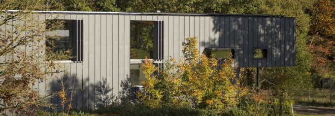 A rectangular building with paneled cladding. Autumnal foliage surrounds the exterior.