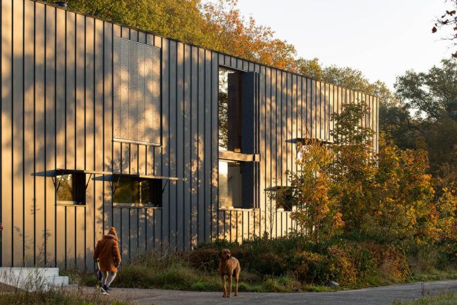 A rectangular building with paneled cladding. A person and a dog stand outside the building.