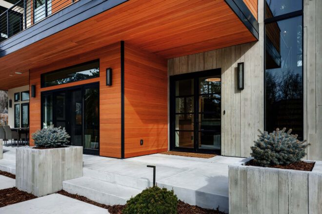 A closeup of the home's entrance, featuring black door and window frames and a paneled orange-tone wood facade.