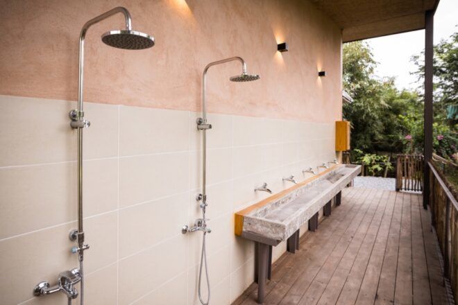 An outdoor shower area with two steel showerheads and a trough sink.