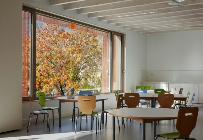 round wood tables and colorful chairs next to large window