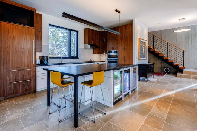 A kitchen area with a black table and two yellow chairs. Wood cabinets surround black and white counters with a sink and oven.