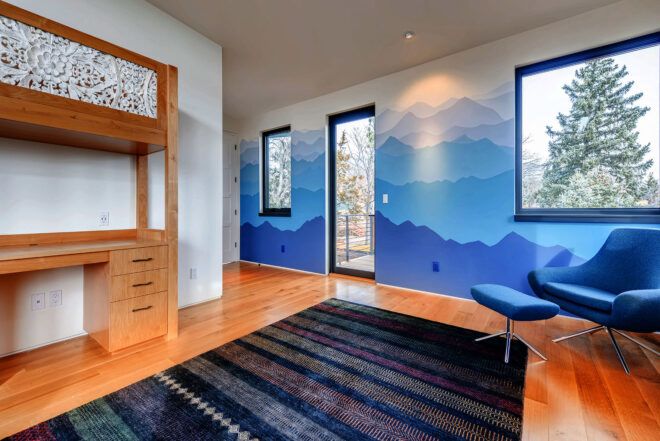 An upstairs bedroom with a two-in-one raised bed and desk. The walls are painted blue to simulate the silhouette of mountains. A blue striped rug covers the floor.