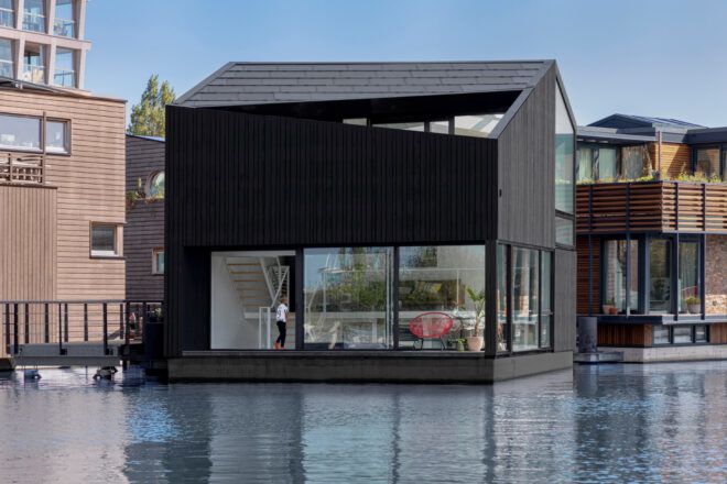 black timber floating home with glass walls on the first floor