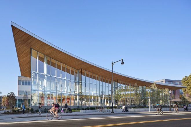 A streetview of a building with a wood-accented, curved roof and windowed facade.