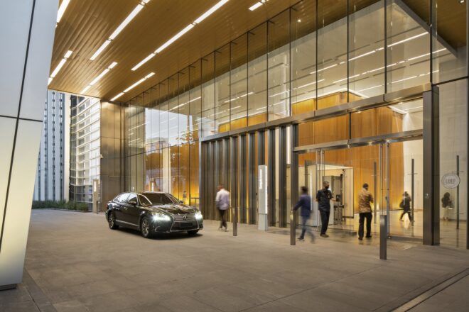 A car parked by the entrance to a large building with a glass facade.