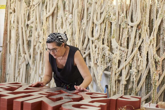 Tanya Aguiñiga working on her window display with a backdrop of off-white ropes behind her.