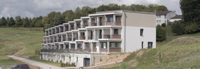 A rolling green landscape with a housing complex with a vertically tiered, off-white facade.