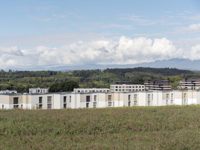A rolling green landscape with a housing complex with an off-white facade.