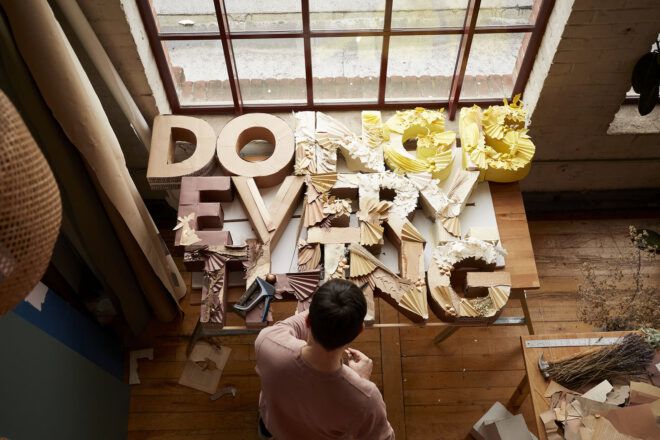 An overhead shot of a person standing next to a table with another artist's "doing is everything" artwork.