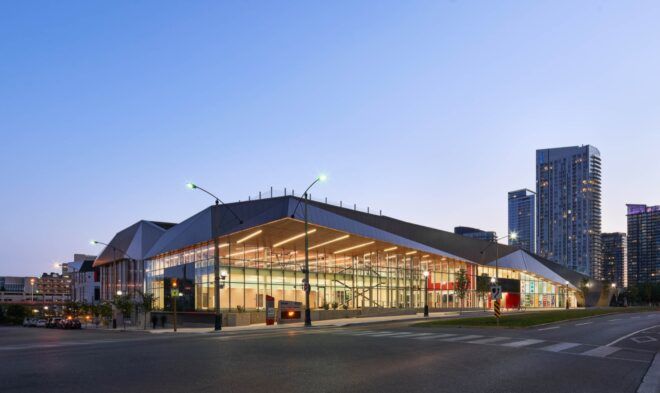 A streetview of a large building with windows, lit up from inside.