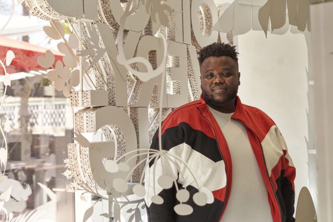 Morel Doucet standing next to his "doing is everything" artwork display for Nespresso.