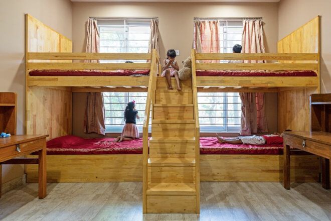 A set of four bunk beds with red sheets and a staircase in the middle.
