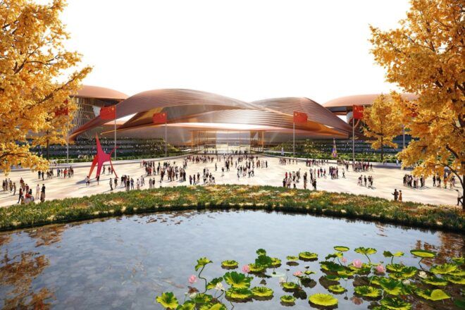 A pond in front of a courtyard where people mill around in front of a large building with curved rooftops.
