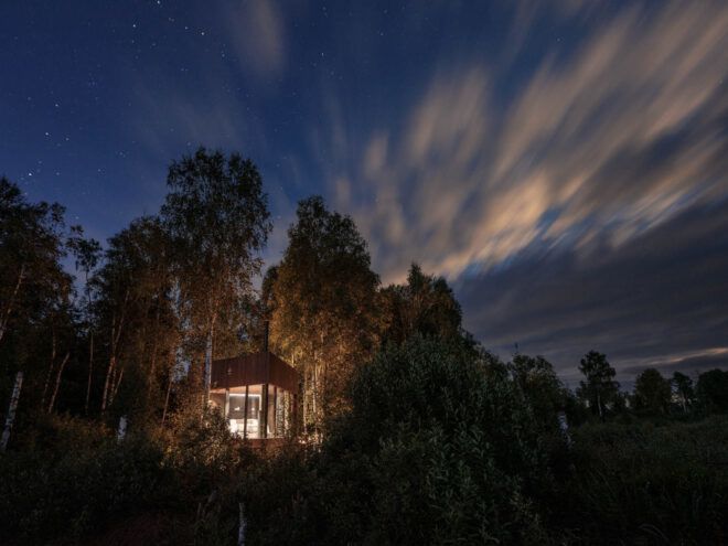 wood and glass cabin lit from within at dusk