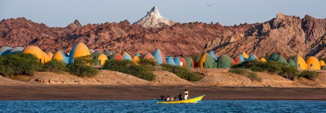 yellow boat on water sailing past community of colorful dome homes