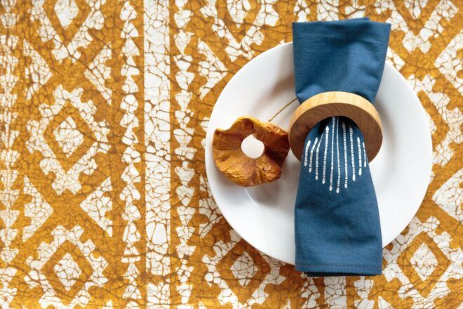 A napkin and napkin ring set on top of a white plate on an orange and white patterned cloth.