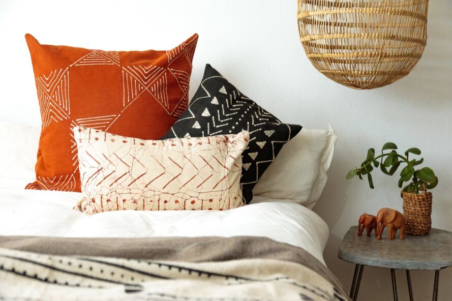 A bed with three decorative throw pillows in white, orange and black patterns.