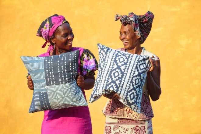Two people holding patterned blue and white throw pillows in front of a yellow background.