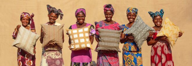 A group of six people holding throw pillows in front of a yellow wall.